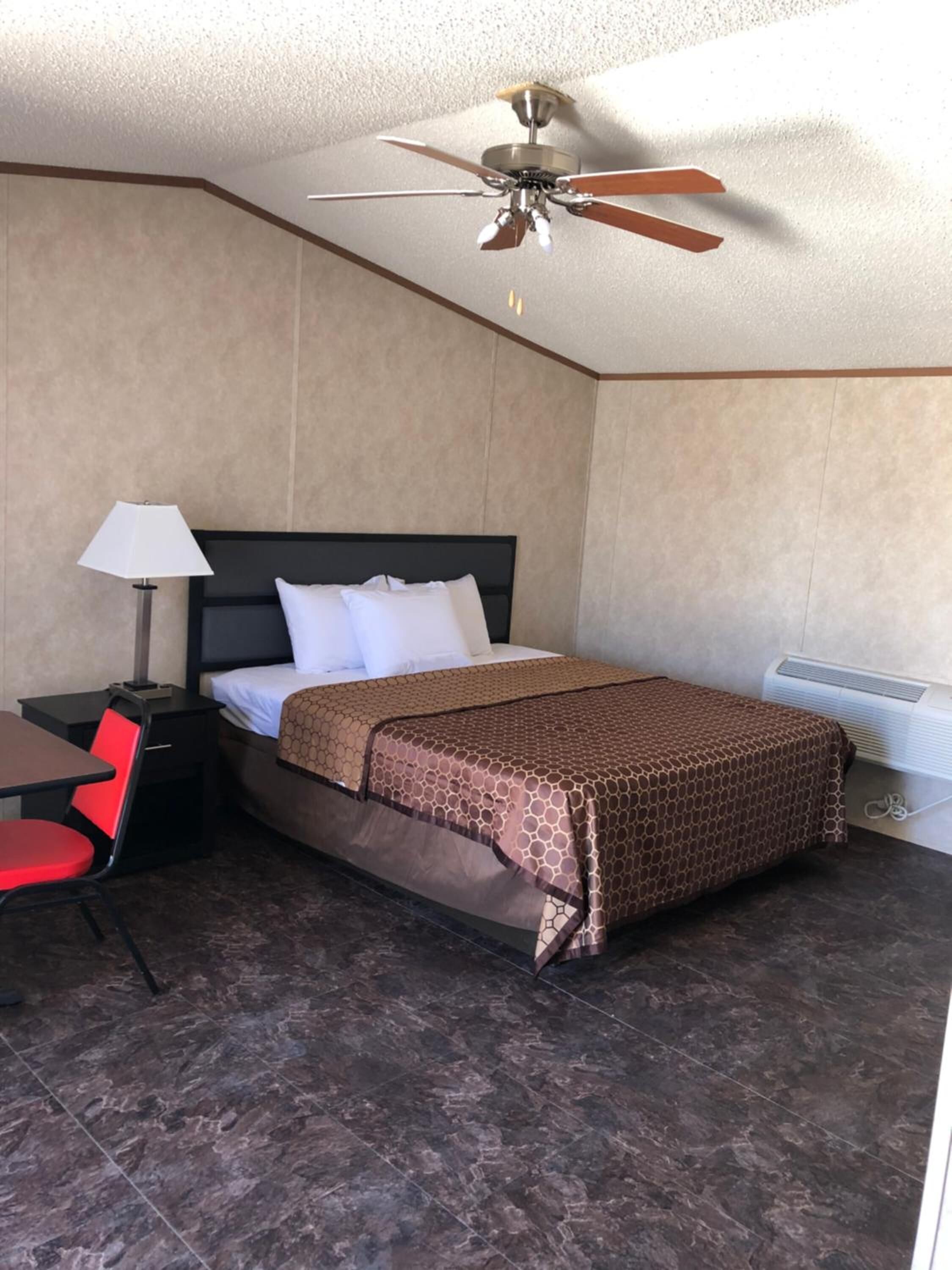 Ein Hotelzimmer mit Bett, Schreibtisch mit Stuhl, Deckenventilator und Heizung.