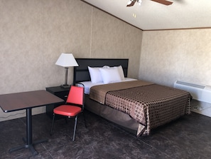Una habitació d'hotel amb un llit, una taula de treball, una cadira, una làmpada i un aparell d'aire condicionat.