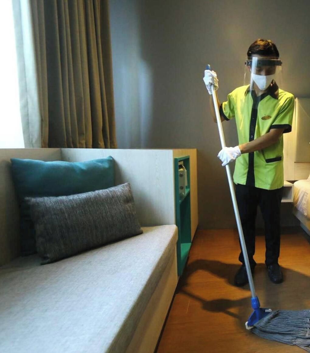A hotel room with a sofa, a bed, and a person cleaning the floor.