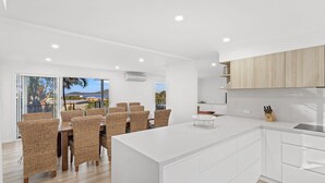 Una cocina moderna con armarios blancos, una isla central y un comedor con sillas de mimbre.