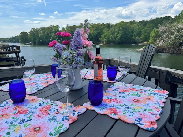 A table set with wine glasses, a bottle, and a vase of flowers on a wooden deck with a view of a lake and forest. - 3 Spacious floors! Great for multiple families (Moneta)