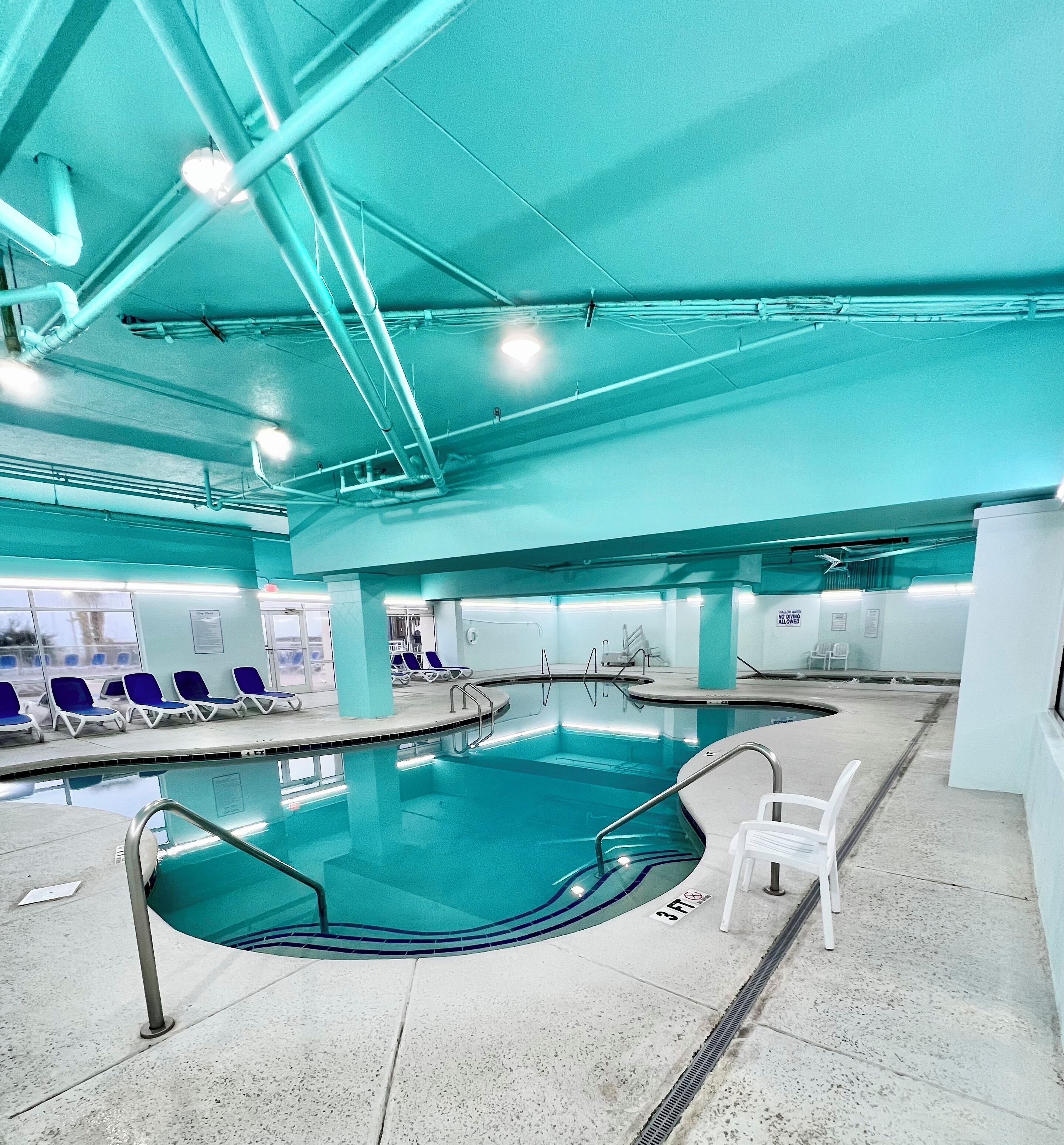 Une grande piscine intérieure dotée de plusieurs couloirs, entourée de chaises longues et recouverte d’un sol carrelé.