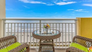 A balcony with wicker furniture, a glass table with a flower vase, and a view of the beach. - Coastal Beachfront Paradise! Resort Style Amenities with a BRAND NEW KITCHEN!! (North Myrtle Beach)