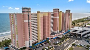 A multi-story hotel with balconies, a parking area, and a view of the beach. - Coastal Beachfront Paradise! Resort Style Amenities with a BRAND NEW KITCHEN!! (North Myrtle Beach)