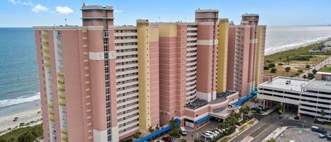 A multi-story hotel with balconies, a parking area, and a view of the beach.