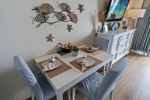 Un coin repas avec une table blanche dressée pour quatre personnes, agrémenté de chaises à rayures, d’une œuvre d’art décorative au mur et d’un meuble contenant un téléviseur.
