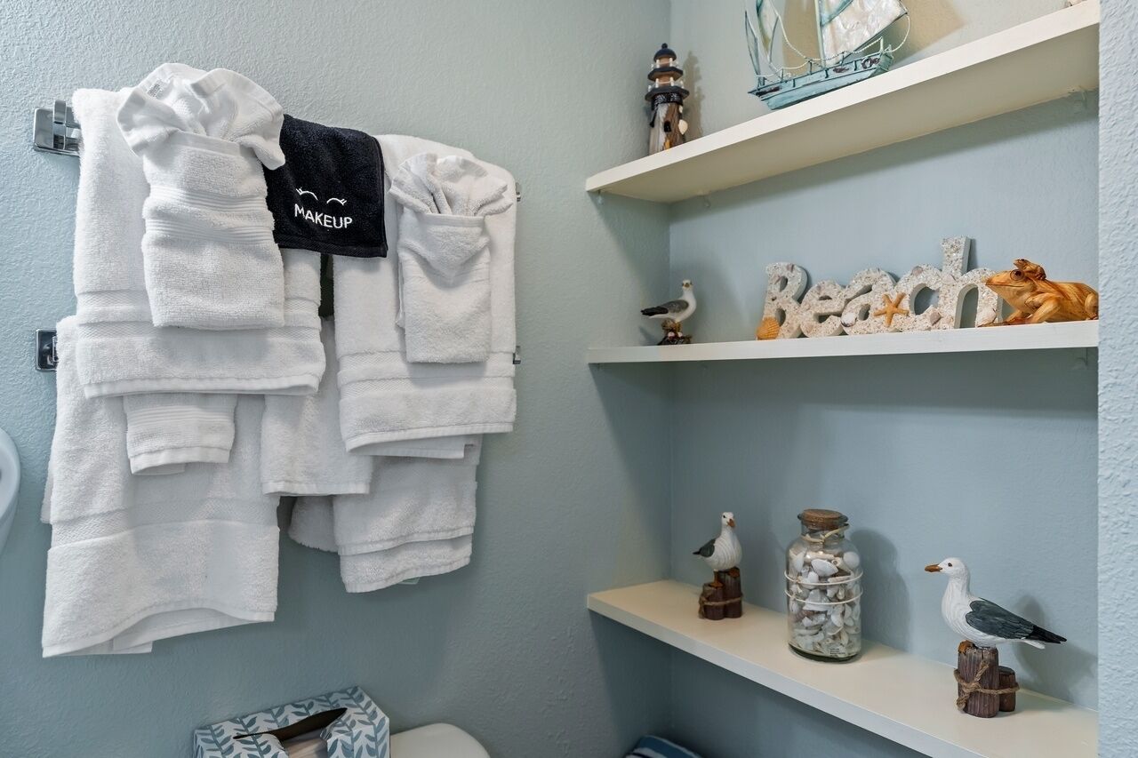 A bathroom with white towels hanging on a rack, a shelf with decorative items, and a toilet visible in the corner.