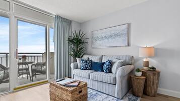 A modern living room with a sofa, a lamp, a plant, and a view through a sliding glass door to the outdoors.