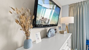 A hotel room with a television mounted on the wall, a vase with dried flowers, a lamp, and a sign indicating no smoking. - Coastal Beachfront Paradise! Resort Style Amenities with a BRAND NEW KITCHEN!! (North Myrtle Beach)
