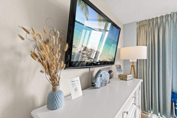 Een hotelkamer met een aan de muur bevestigde televisie, een vaas met gedroogde bloemen, een lamp en een bordje met de tekst rookvrij.