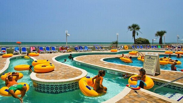 A pool area with multiple swimming pools, lounge chairs, and people using inflatable rings. - Coastal Beachfront Paradise! Resort Style Amenities with a BRAND NEW KITCHEN!! (North Myrtle Beach)