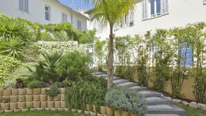 Ein Wohngarten mit einer Steintreppe, verschiedenen Pflanzen und einem weißen Gebäude mit Fensterläden.