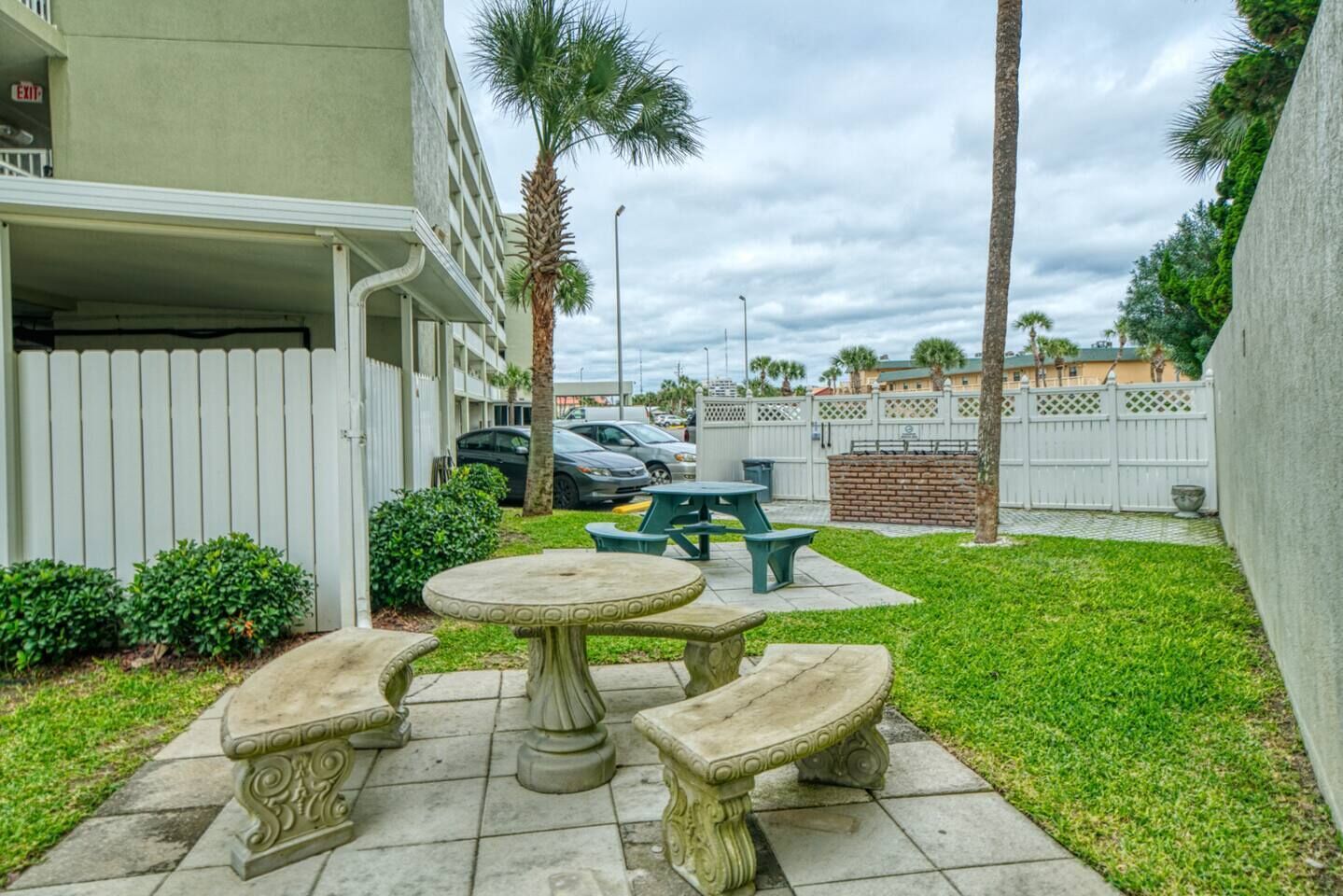 A courtyard with a white fence, palm trees, and a picnic table with benches.