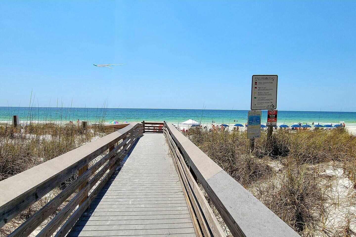 A wooden boardwalk leading to a beach with clear skies and a distant airplane.