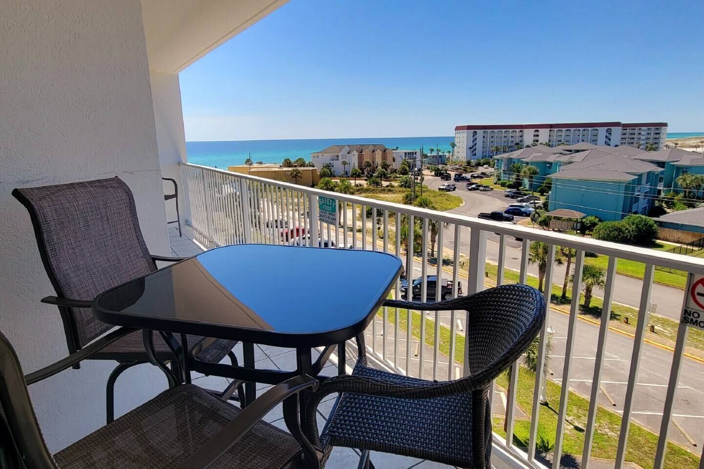 A balcony with a table and chairs, overlooking a beach and hotel buildings.