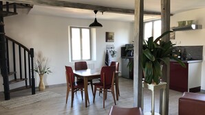 Un comedor con mesa y sillas de madera, una escalera y una cocina al fondo.