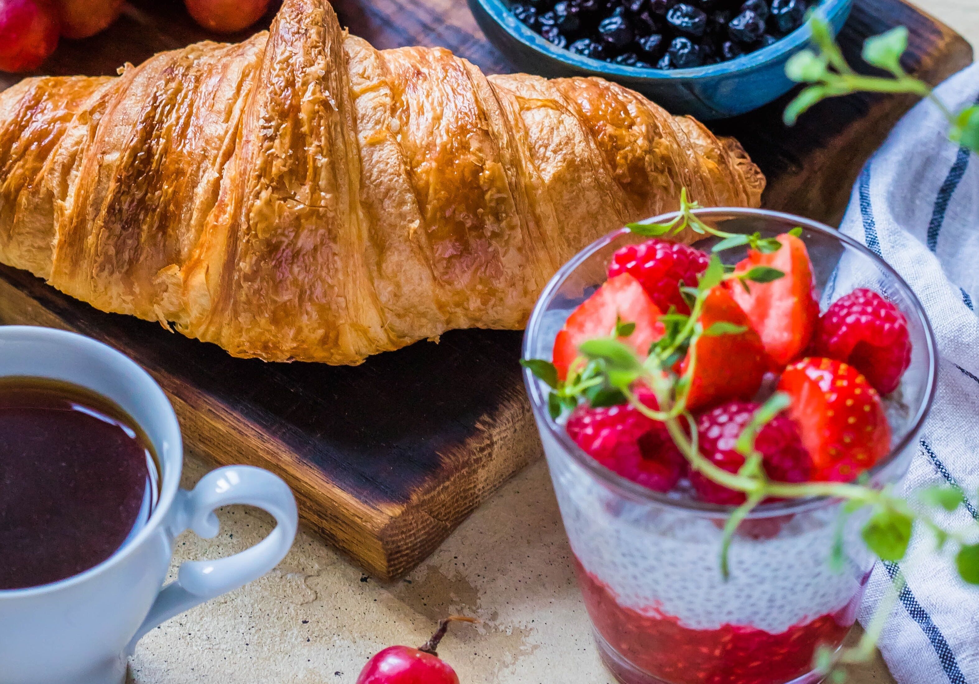 A croissant, a glass of red fruit juice, and a cup of coffee on a wooden surface.