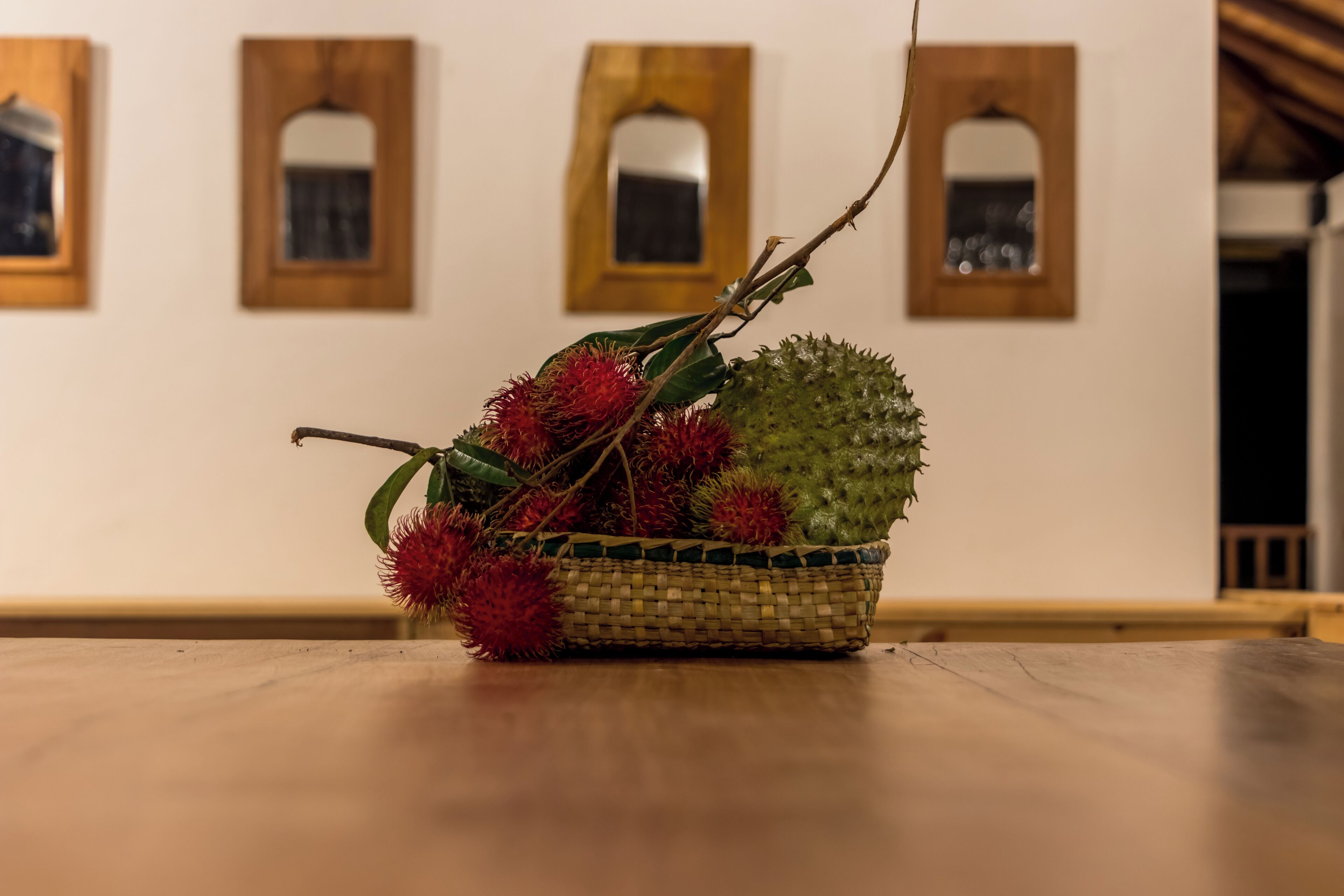 Uma cesta de vime com uma fruta verde e frutos vermelhos e espinhosos sobre uma mesa de madeira.