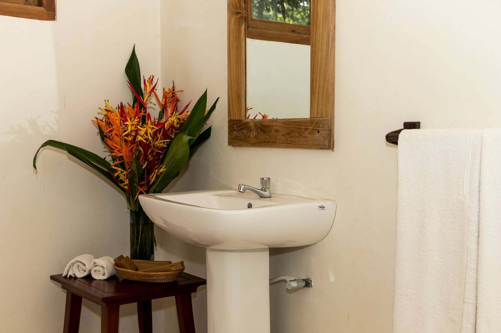 Une salle de bain avec un lavabo blanc, un miroir à cadre en bois, un vase rempli de fleurs colorées et un porte-serviettes.