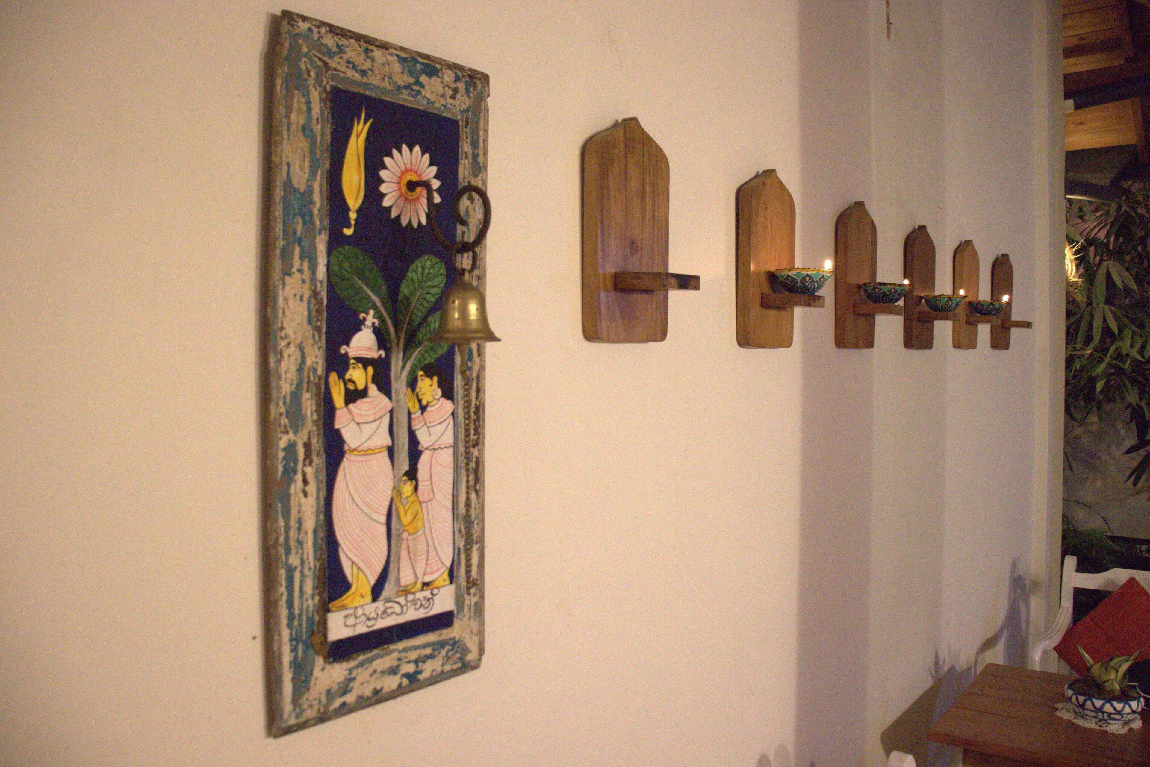 A wall with a framed painting, wooden wall-mounted shelves with candles, and a table with a bowl.