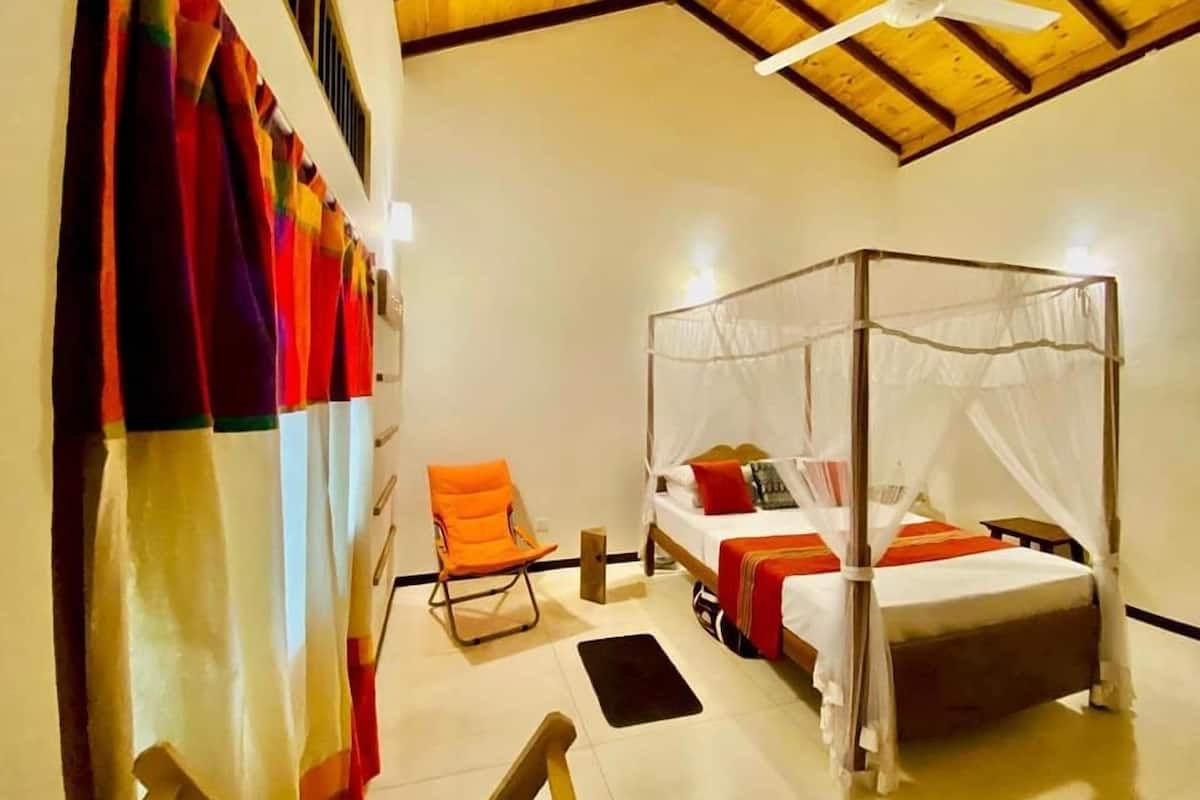 Ein Schlafzimmer mit Himmelbett, Sessel und Deckenventilator.