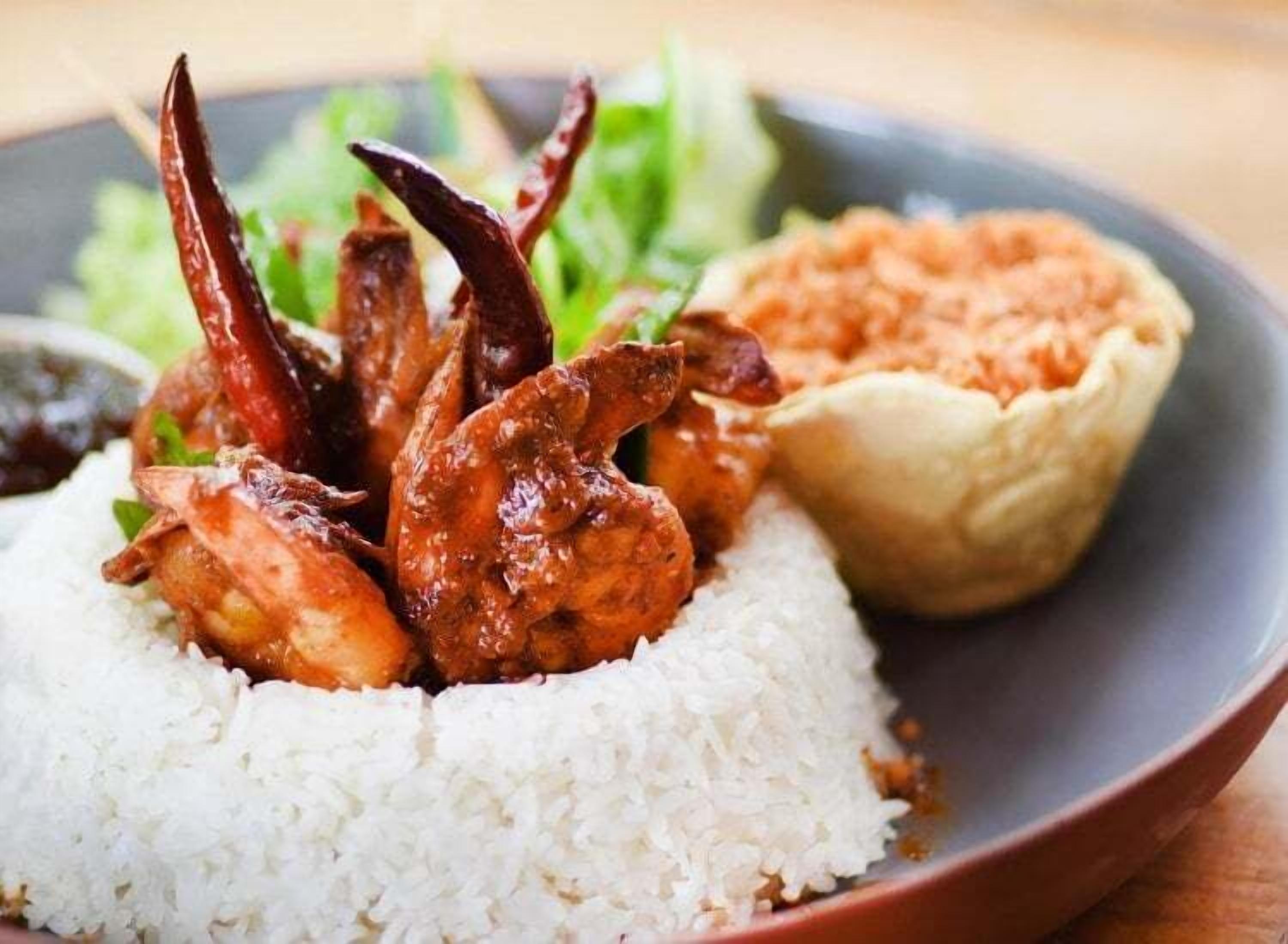 A plate with white rice, grilled chicken, a small bowl of sauce, and a side of greens.