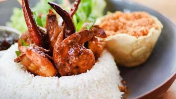 A plate with white rice, grilled chicken, a small bowl of sauce, and a side of greens.
