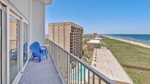 Ein Balkon mit blauen Adirondack-Stühlen, mit Blick auf einen Strand und einen Poolbereich.