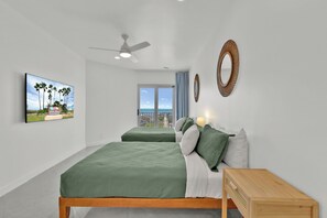 Une chambre moderne avec deux lits, un ventilateur de plafond, une grande fenêtre offrant une belle vue et un téléviseur fixé au mur.