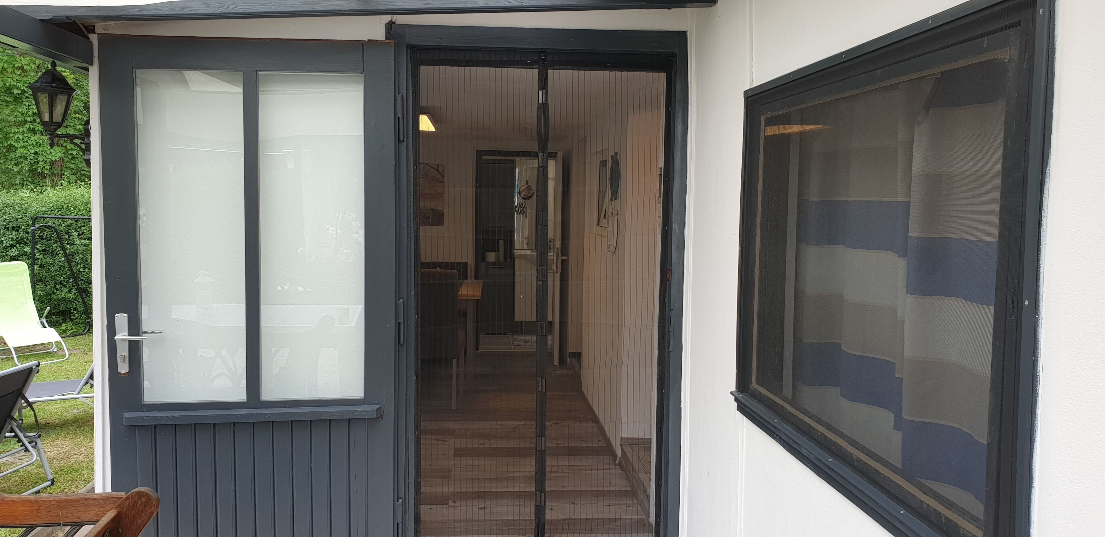 En hall med en dörr som leder in till ett rum, en stol utanför och ett fönster med persienner.