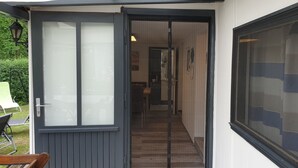 A hallway with a door leading to a room, a chair outside, and a window with blinds. - Great bungalow on the water (terrace, garden, beach, boat, bicycles, etc.) (Groß Kreutz (Havel))