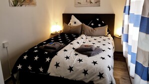 A neatly made bed with star-patterned bedding, a nightstand with a lamp, and a motivational poster on the wall. - Great bungalow on the water (terrace, garden, beach, boat, bicycles, etc.) (Groß Kreutz (Havel))