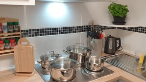 A kitchen with stainless steel pots on the stove, a wooden cutting board, a spice rack, and a potted plant on the countertop. - Great bungalow on the water (terrace, garden, beach, boat, bicycles, etc.) (Groß Kreutz (Havel))