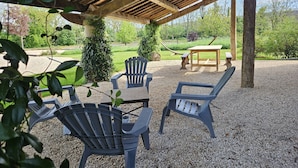 An outdoor patio with wooden beams, a table, and two Adirondack chairs.