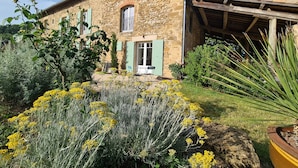 A stone house with a garden in front, featuring yellow flowers and green shrubs.