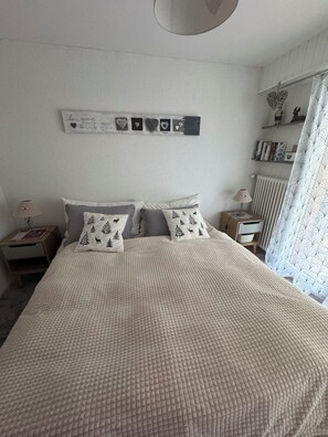 A bedroom with a large bed, two bedside tables, a wall-mounted shelf with decorative items, and a window with curtains. - Nendaz Centre Superbe Appartement 3 p. 75m2 Avec Piscine Parking et vue (Nendaz)