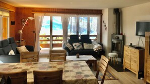 A cozy living room with a sofa, dining table, and chairs. There is a fireplace and a television. - Nendaz Centre Superbe Appartement 3 p. 75m2 Avec Piscine Parking et vue (Nendaz)