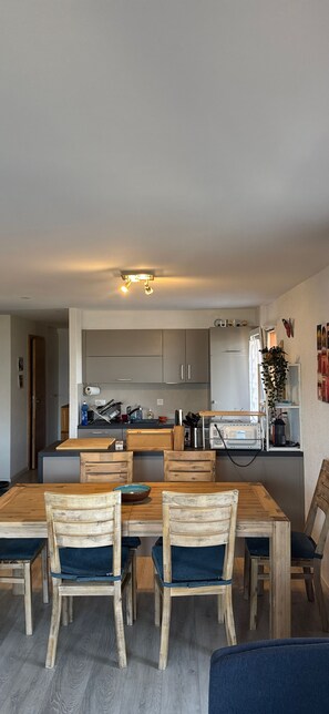 A modern kitchen with wooden cabinets, a dining table with chairs, and a small island with appliances. - Nendaz Centre Superbe Appartement 3 p. 75m2 Avec Piscine Parking et vue (Nendaz)