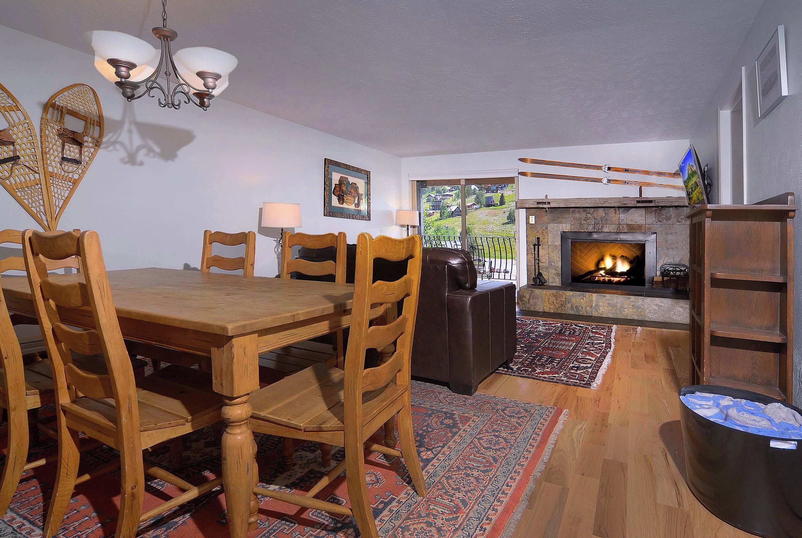 A dining area with a wooden table and chairs, a fireplace, and a view of the outdoors.