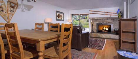 A dining area with a wooden table and chairs, a fireplace, and a view of the outdoors.