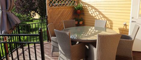 Une terrasse avec des chaises en osier et une table en verre, entourée d’une clôture en bois et d’un mur jaune.