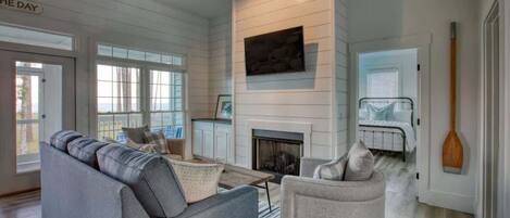 A modern living room with a fireplace, a sofa, a chair, and a view of the outdoors.