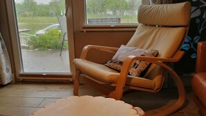 Huoneessa on suuri ikkuna, pehmusteella varustettu puinen keinutuoli ja pieni puinen pöytä, jonka muotoilu on ainutlaatuinen.