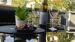 Une table en verre avec une bouteille de vin et deux verres à vin, une plante en pot et une petite assiette contenant de la nourriture.