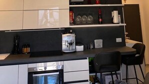 Une cuisine moderne équipée d’un four encastré, d’une machine à café et d’un coin repas avec deux chaises.