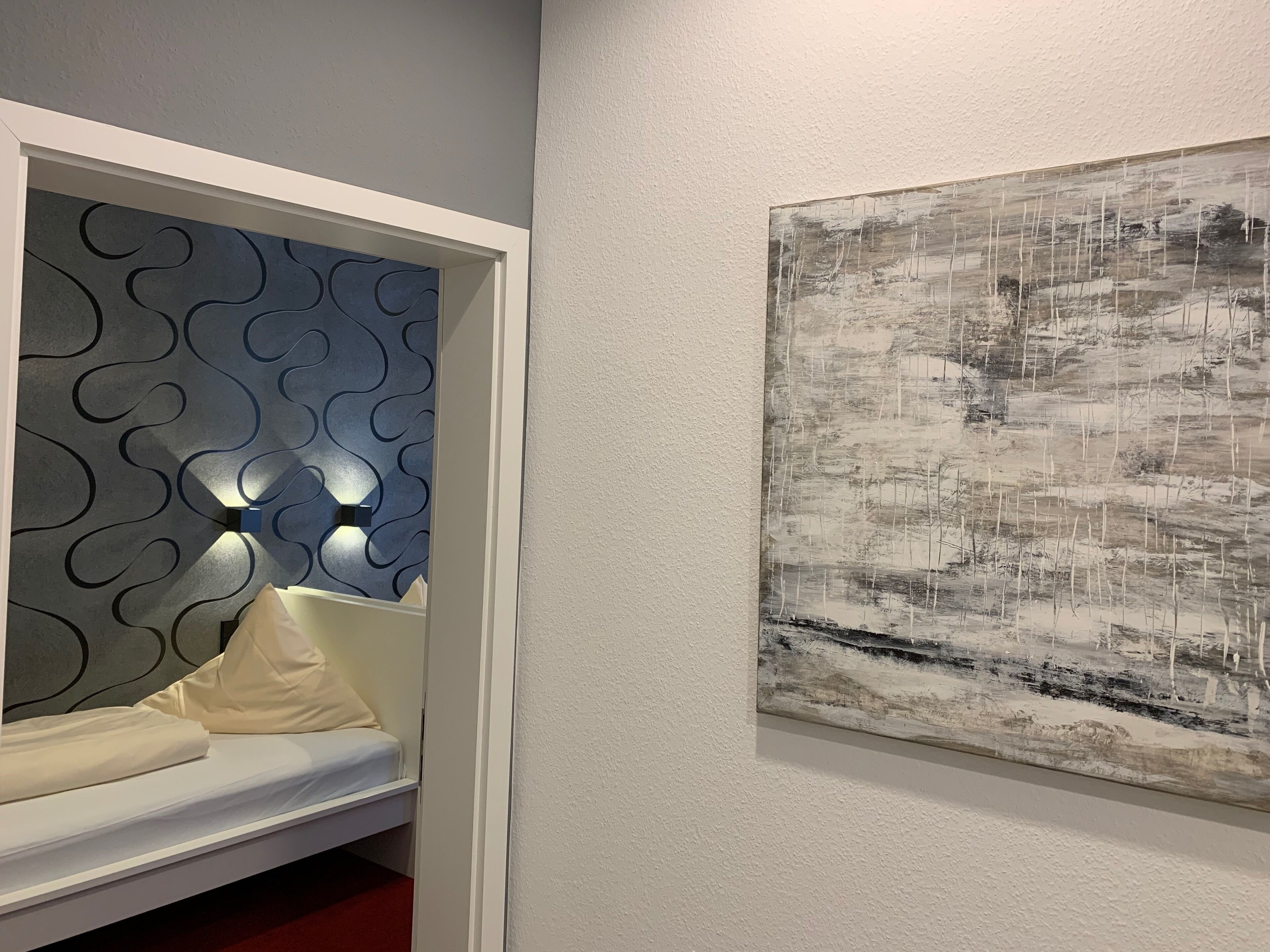A room with a bed, a wall-mounted light fixture, and a large abstract painting.