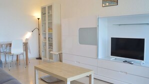 A modern living room with a flat-screen TV, a white cabinet, and a dining area with chairs and a table. - Family apartment sleeps 6 Banyuls-sur-Mer A/C, private parking, near beaches (Banyuls-sur-Mer)