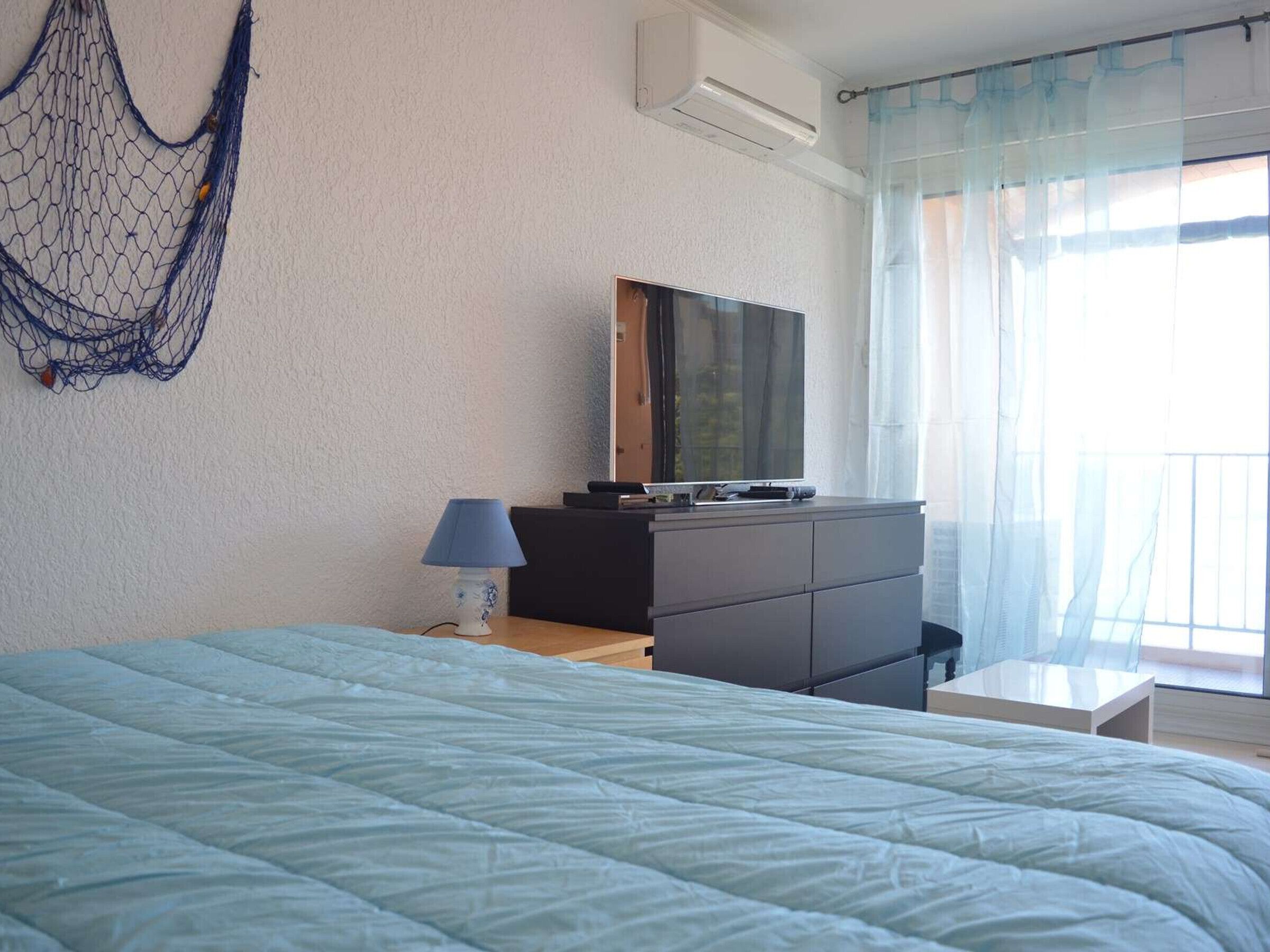 Une chambre à coucher avec un lit, une commode, un téléviseur et une fenêtre avec des rideaux.