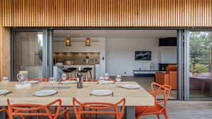 Un espace repas moderne avec une table en bois dressée pour quatre personnes, des chaises orange et une cuisine en arrière-plan.