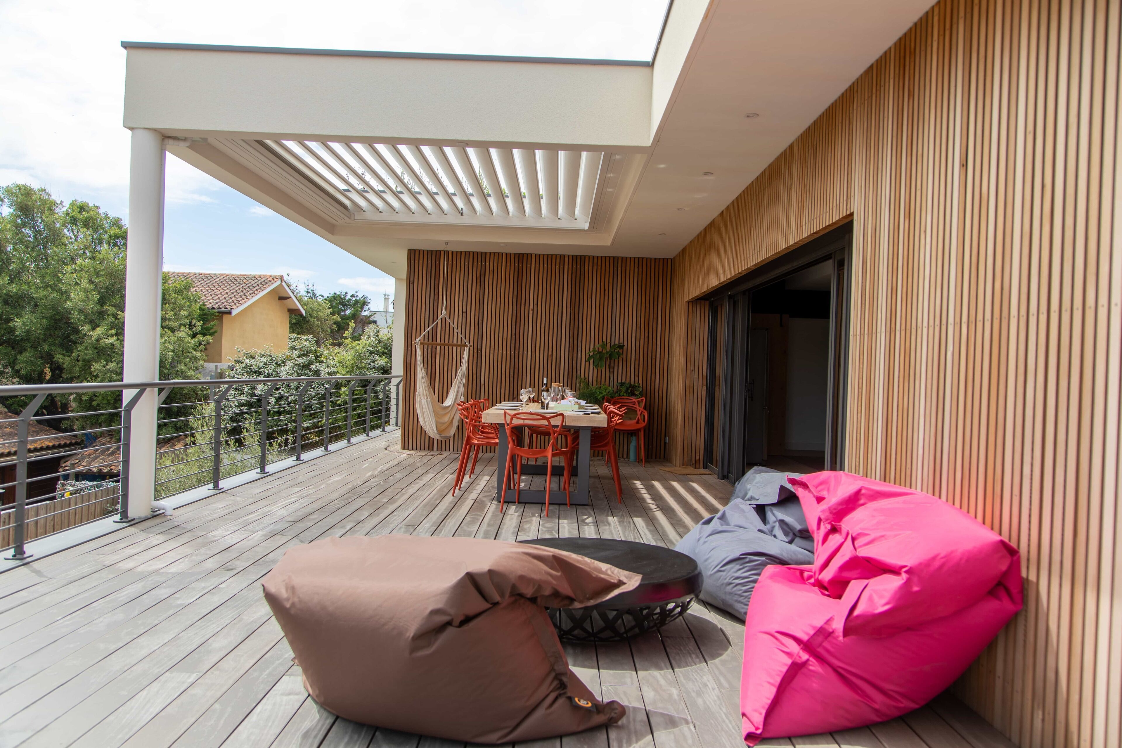 Une terrasse extérieure moderne, dotée d’une plateforme en bois, d’une table à manger avec des chaises et de deux fauteuils en forme de sac.